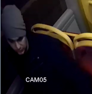 Na zdjęciu widać mężczyznę podróżującego autobusem. Mężczyzna ubrany jest w szarą czapkę i zajmuje miejsce siedzące obok okna. Na zdjęciu widoczny jest napis &quot;CAM 05&quot;.