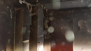 Zdjęcie przedstawia wnętrze mieszkania, widać drzwi wejściowe i ściany zniszczone w wyniku pożaru