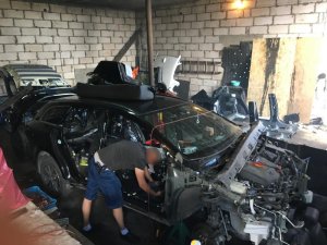 Zdjęcie przedstawia wnętrze garażu z zdemontowanym częściowo pojazdem. Przy samochodzie pochyla się policjant w cywilnym ubraniu