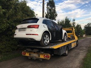 Zdjęcie przedstawia lawetę, na której umieszczony jest białe audi. Samochód ma zaklejoną czarną taśmą prawą stronę, w miejscu drzwi.