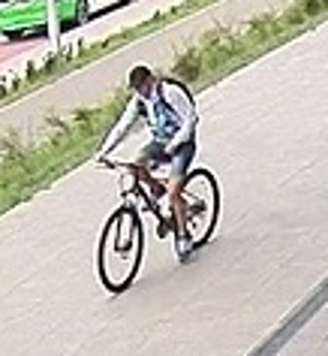 na zdjęciu widać mężczyznę jadącego rowerem po chodniku, na ramionach widać paski od plecaka