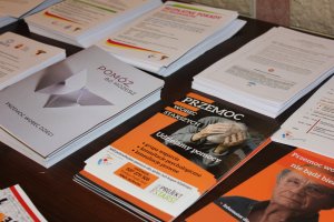 Zdjęcie przedstawia kilka rodzajów kolorowych ulotek ułożonych na blacie brązowego stołu. Wszystkie tytuły odnoszą się do kwestii przemocy.