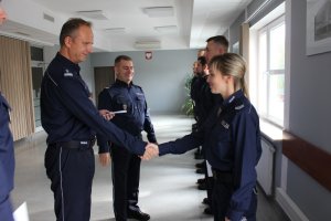 Zdjęcie przedstawia stojących w rzędzie policjantów w granatowych mundurach służbowych. Komendant podaje rękę jednej z policjantek.
