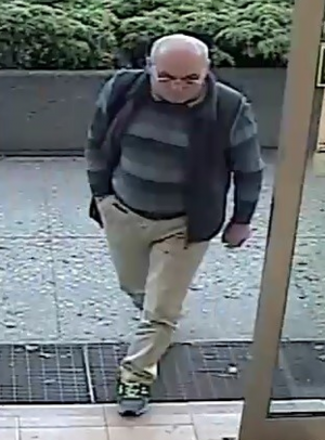 Zdjęcie przedstawia mężczyznę wchodzącego do sklepu, jest on w wieku około 50-60 lat, ma okulary na twarzy, ubrany jest w sweter w paski, ciemną kamizelkę, jasne spodnie. Mężczyzna posiada czarną torbę przewieszoną przez prawe ramię. Prawą rękę trzyma w kieszeni spodni.