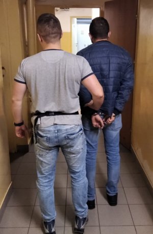 Na zdjęciu widać policjanta w ubraniu cywilnym z zatrzymanym mężczyzną w kajdankach