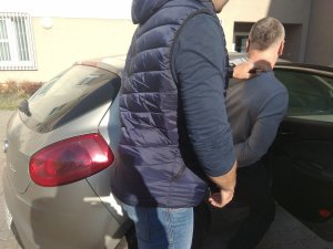 Na zdjęciu widać policjanta po cywilnemu i zatrzymanego mężczyznę wsiadającego do radiowozu nieoznakowanego