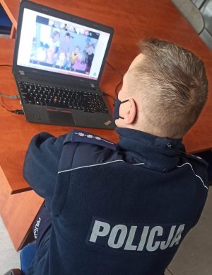 na zdjęciu widać dzielnicowego prowadzącego zajęcia przed laptopem