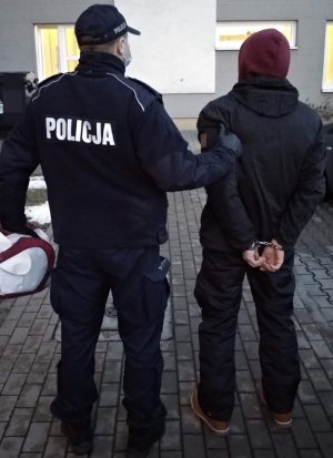 na zdjęciu widać policjanta w mundurze i zatrzymanego mężczyznę w kajdankach