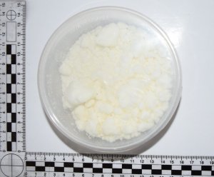 Zdjęcie przedstawia okrągły przezroczysty pojemnik zawierający białą zbrylowaną substancję.