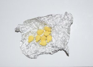 Zdjęcie przedstawia osiem żółtych tabletek, które leżą na fragmencie folii aluminiowej.
