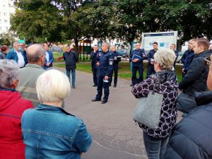 Zdjęcie przedstawia mieszkańców, którzy stoją na debacie. Przed nimi stoją policjanci w umundurowaniu służbowym. Spotkanie odbywa się na świeżym powietrzu.