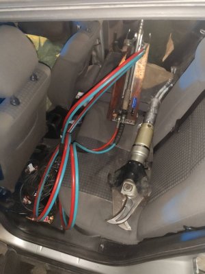 Zdjęcie przedstawia wnętrze samochodu. Na tylnej kanapie obitej szarym pokrowcem widać narzędzie, z którego odchodzą czerwone i niebieskie grube przewody.