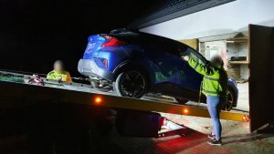 Zdjęcie przedstawia odzyskany przez policjantów samochód, który znajduje się na lawecie. Po jej obu stronach widać dwóch pracowników.