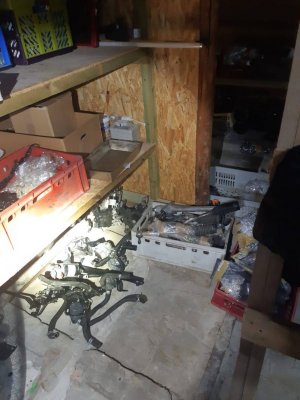 Zdjęcie przedstawia pomieszczenie garażowe, a w nim rozłożone na ziemi części samochodowe.
