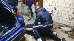 Policjant przytrzymuje leżącego na ziemi mężczyznę.