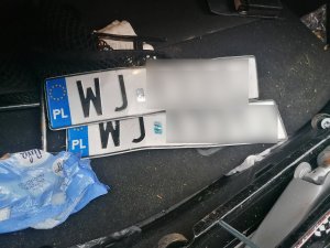 Wnętrze bagażnika, a w środku foliowa torebka i dwie tablice rejestracyjne.