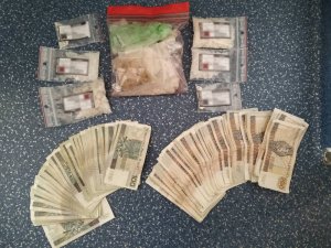 Zdjęcie przedstawia leżące na stole pieniądze ułożone w wachlarze oraz nielegalne środki spakowane w małe przezroczyste torebeczki.