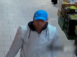 Zdjęcie przedstawia mężczyznę wewnątrz sklepu.  Jest to mężczyzna w wieku ok 35 lat, ubrany w kurtkę koloru białego, czapkę z daszkiem w kolorze niebieskim.