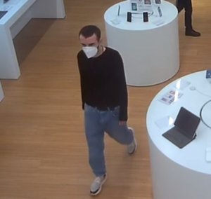 Zdjęcie przedstawia wnętrze sklepu a w nim mężczyznę w wieku około 30 lat, wzrostu około 175 cm, szczupłej budowy ciała, ma on ciemne krótkie włosy z wyraźnymi zakolami, ciemny zarost widoczny spod założonej maseczki ochronnej; ubrany jest w czarną bluzkę z długimi rękawami, szerokie spodnie jeansowe w kolorze niebieskim z czarnym paskiem, białe obuwie sportowe.