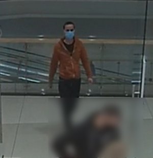 Zdjęcie przedstawia wnętrze sklepu, a w nim mężczyznę w wieku ok 30 lat,  wzrostu około 180 cm, ma on krótkie ciemne włosy, ubrany jest w rozpinaną bluzę w kolorze pomarańczowym, spodnie w kolorze czarnym, na twarzy ma maseczkę ochronną.