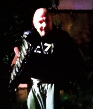 Zdjęcie przedstawia mężczyznę w wieku około 45 lat, krępej budowy ciała, łysy, ubrany w ciemną kurtkę pikowaną, jasne spodnie i ciemną bluzę.