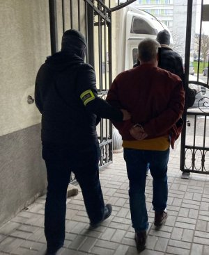 Na zdjęciu znajduje się poszukiwany mężczyzna, który jest prowadzony przez Policjanta.