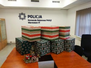 Zdjęcie przedstawia prezenty opakowane w kolorowy papier i ułożone na biurku. W tle na ścianie widać napis &amp;quot;Komenda Rejonowa Policji Warszawa VI&amp;quot;.