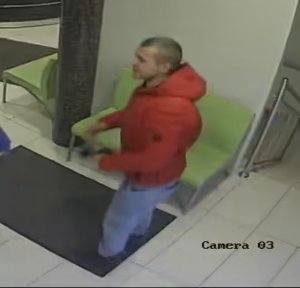 Zdjęcie przedstawia mężczyznę w czerwonej kurtce i niebieskich spodniach jeansowych. W tle widać wyposażenie pomieszczenia w postaci zielonych mebli.