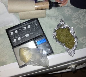 Zdjęcie przedstawia nielegalne środki, które leżą na blacie białej pralki - biała substancja znajduje się w prześwitującej torebce, jest umieszczona na domowym kalkulatorze, obok leży zawiniątko z folii aluminiowej, a w niej zieloną substancję. Obok leżą kosmetyki.