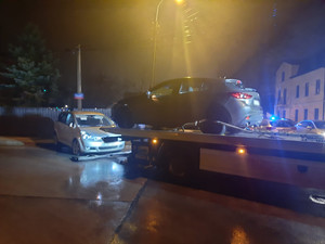 Zdjęcie jest zrobione nocą. Widać na nim dwa pojazdy na ulicy, jeden koloru srebrnego m-ki Toyota stoi przodem do lawety, na lawecie umieszczony jest pojazd m-ki Mazda.