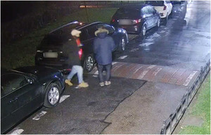 Zdjęcie przedstawia dwóch mężczyzn stojących obok dwóch zaparkowanych pojazdów. Pierwszy z nich ubrany jest w granatową kurtkę z futrzanym kapturem, jeansowe spodnie i brązowe buty.

Drugi mężczyzna ma czarną kurtkę, jeansowe spodnie, brązowe buty, czapkę z daszkiem w jasnym kolorze. Zdjęcie jest wykonane nocą. Obaj stoją tyłem do kamery monitoringu.