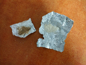 Zdjęcie przedstawia dwa zawiniątka z folii aluminiowej, w jednym znajduje się biały środek, w drugim beżowy
