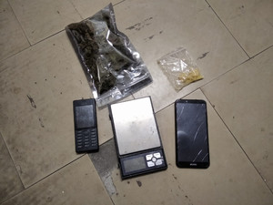 Zdjęcie przedstawia zabezpieczone środki znajdujące się w foliowych torebkach oraz dwa czarne telefony komórkowe i wagę elektroniczną leżącą na ziemi.