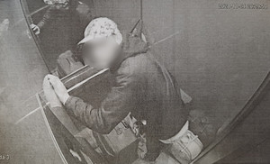 Zdjęcie przedstawia mężczyznę w windzie. Zdjęcie jest szare, pochodzi z kamery monitoringu.