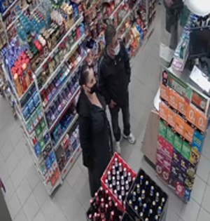 Zdjęcie przedstawia wnętrze sklepu. Widać w nim kobietę i mężczyznę, są w wieku około 45-55 lat, oboje prawdopodobnie narodowości romskiej.
Kobieta ma otyłą sylwetkę, ubrana była w czarną spódnicę, białe buty, czarną koszulę lub marynarkę, twarz zasłaniała jej czarna maseczka.
Mężczyzna jest normalnej budowy ciała, ubrany w czarne buty, czarne spodnie jeansowe, czarny bezrękawnik oraz granatowy t-shirt. Na twarzy ma jasną maseczkę ochronną. W tle widać półki i regały z asortymentem.