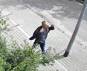 Zdjęcie przedstawia idącego chodnikiem mężczyznę w wieku około 40-45, normalnej budowy ciała, ma siwe włosy, czesane na bok, ubrany jest w spodnie jeansowe koloru niebieskiego, niebieską koszulkę z krótkim rękawem oraz czarną kurtkę.