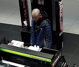 Zdjęcie przedstawia mężczyznę wewnątrz drogerii. Mężczyzna jest w wieku około 25-30 lat, szczupłej budowy ciała, ubrany był w czarną bluzkę z kapturem, niebieską kurtkę z kapturem.