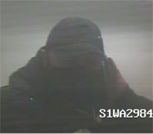 Zdjęcie jest z kamery monitoringu. Widać na nim ciemną sylwetkę mężczyzny ubranego w czapkę z daszkiem.