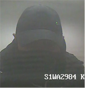Zdjęcie jest z kamery monitoringu. Widać na nim ciemną sylwetkę mężczyzny ubranego w czapkę z daszkiem. Dolną część twarzy zasłania mu czarna maseczka bądź komin.
