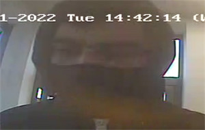 Zdjęcie jest z kamery monitoringu. Widać na nim ciemną sylwetkę mężczyzny, który ma kaptur na głowie. Dolną część twarzy zasłania mu czarna maseczka bądź komin.