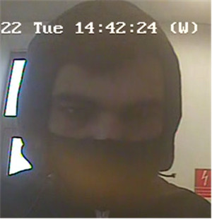 Zdjęcie jest z kamery monitoringu. Widać na nim ciemną sylwetkę mężczyzny, który ma kaptur na głowie. Dolną część twarzy zasłania mu czarna maseczka bądź komin.