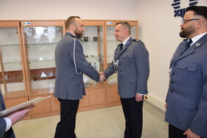 Zdjęcie przedstawia trzech policjantów w galowych mundurach, jeden z nich podaje rękę wyróżnionemu policjantowi.