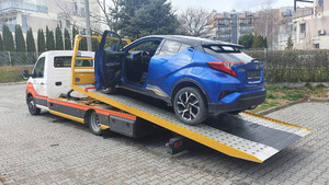 Zdjęcie przedstawia stojący na lawecie odzyskany pojazd m-ki Toyota koloru niebieskiego. Samochód ma otwarte drzwi kierowcy.