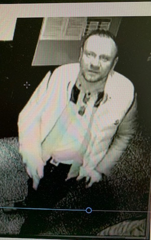 Zdjęcie jest czarno-białe przedstawia mężczyznę, który stoi przodem do kamery i wpatruje się w nią