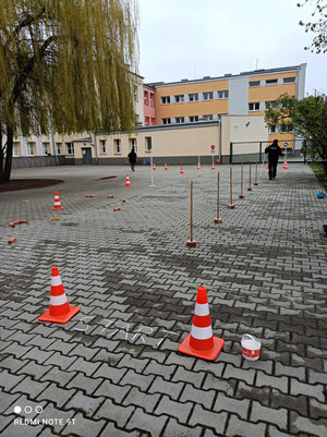 Zdjęcie przedstawia przygotowany tor do egzaminu na kartę rowerową z ustawionymi pachołkami przy którym widać umundurowanych policjantów.