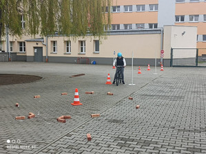 Zdjęcie przedstawia dziecko w kasku na głowie, które jedzie po wyznaczonym torze na rowerze.