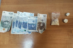 Zdjęcie przedstawia ułożone na stole banknoty: jeden 100-złotowy, kilka 50-złotowych i jeden 10-złotowy, po ich prawej stronie widać przezroczystą torebeczkę z zapięciem strunowym z białą zbrylowaną substancją i dwa okrągłe zawiniątka z jasną substancją.