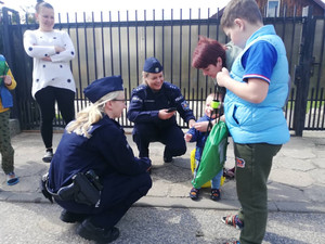 Zdjęcie przedstawia dwie policjantki w mundurach, które kucają przy małym dziecku trzymanym przez inną kobietę.