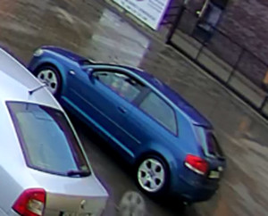 Zdjęcie przedstawia niebieski samochód, po stronie kierowcy siedzi osoba. Obok widać zaparkowany inny pojazd w kolorze srebrnym.
