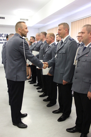 Zdjęcie przedstawia funkcjonariuszy stojących naprzeciwko siebie i podających sobie ręce, są oni ubrani w uroczyste mundury.